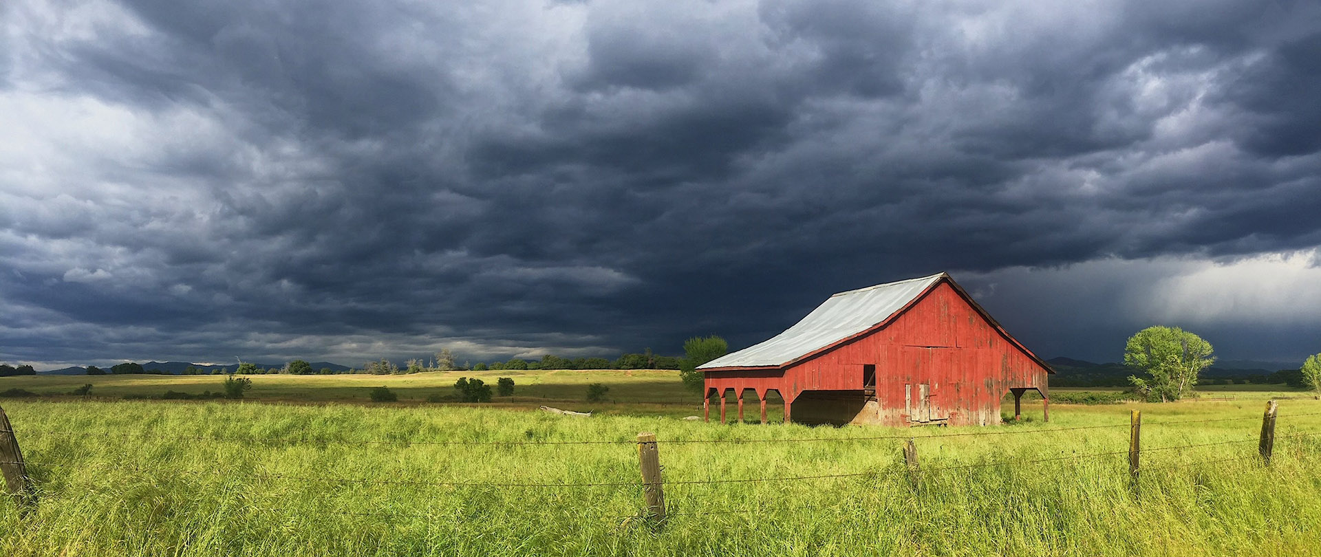 A red barn in a field beneath a stormy sky