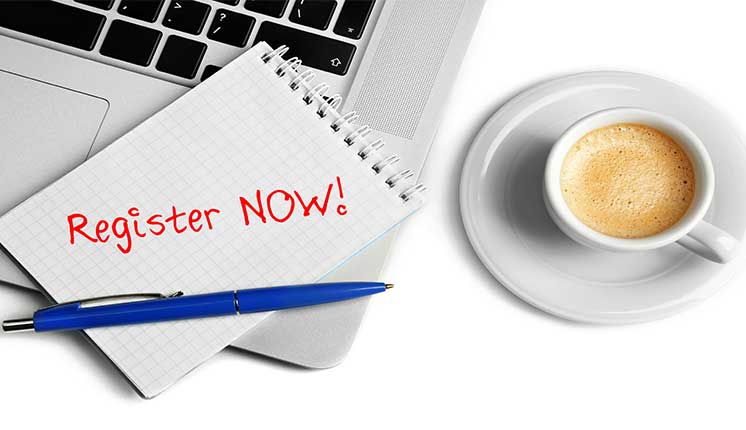 pen and paper resting on corner of laptop next to cup of coffee