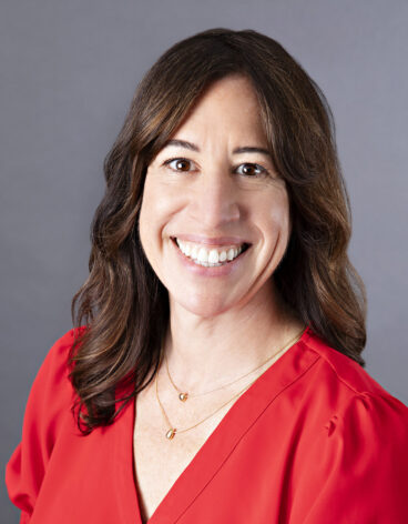 Woman smiling with brown hair and a red blouse.