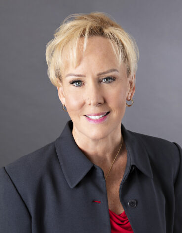Woman smiling with short blonde hair and a black blazer.