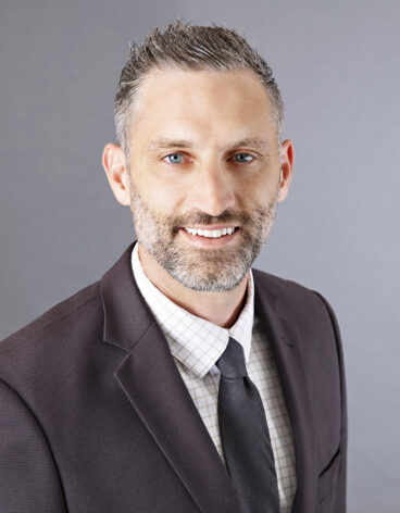 Man smiling wearing a dark blazer and tie.