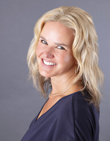 Woman smiling with shoulder length blonde hair and a navy blouse.