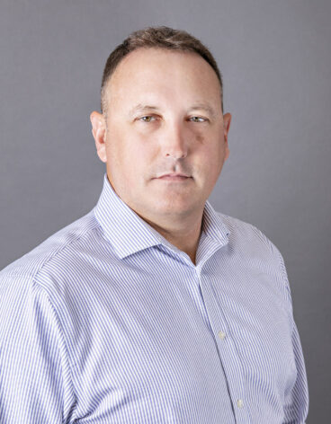 Man with short brown hair and a light blue button up shirt.