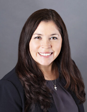 Woman smiling with long dark hair and a dark blazer.