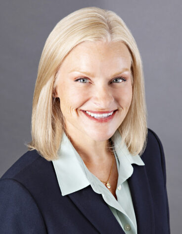 Woman smiling with blonde hair and a navy blazer.