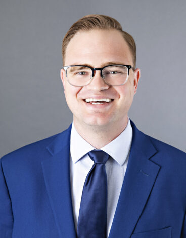 Man smiling with short light brown hair and a bright blue blazer and tie.