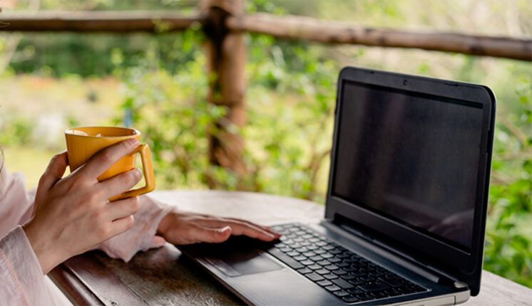 Hand holding coffee cup while typing on a laptop.