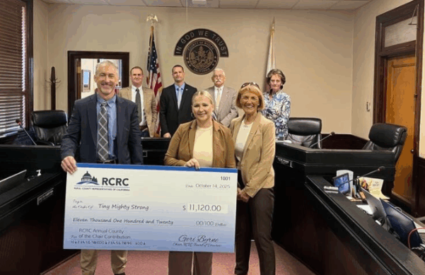 Individuals holding a large check smiling inside a board room.