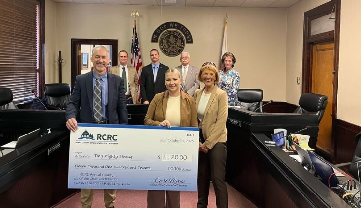 Individuals holding a large check smiling inside a board room.