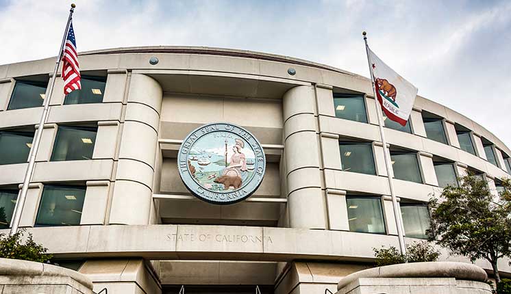 Building of the CPUC with California State Seal affixed on front and American and State flags to the side of the entrance