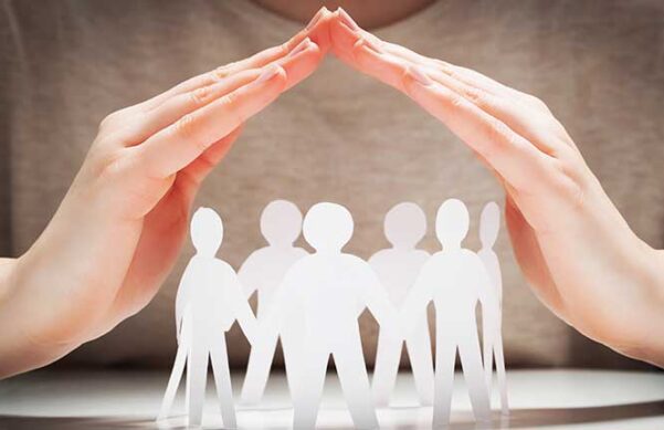 paper cutouts of people standing under hands forming a protective covering.