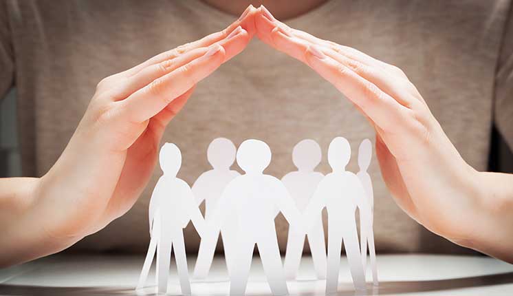paper cutouts of people standing under hands forming a protective covering.