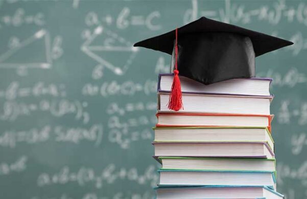 graduation cap stacked on books, chalkboard blurred in background