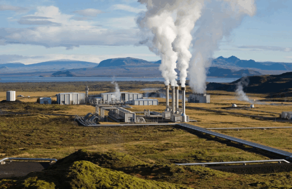 geothermal facility with white smoke disseminating from a few smoke stacks in a green field.