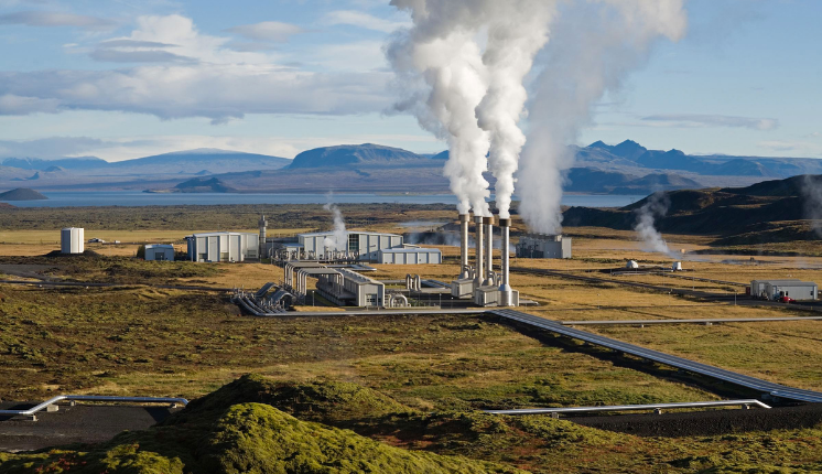 geothermal facility with white smoke disseminating from a few smoke stacks in a green field.