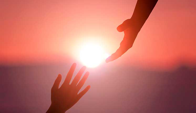 hands reaching for each other against a sunset backdrop