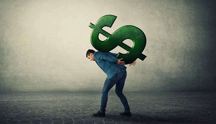 man hunched over carrying a huge green dollar sign on his back