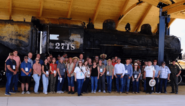 A group of people stand smiling in front of a train engine.