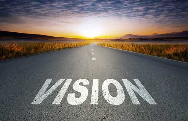 the word "Vision" on top of a road with fields beside and distant mountains awash in the light of the rising sun