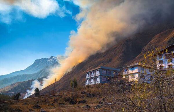 houses on a hillside with wildfire smoke billowing into the air