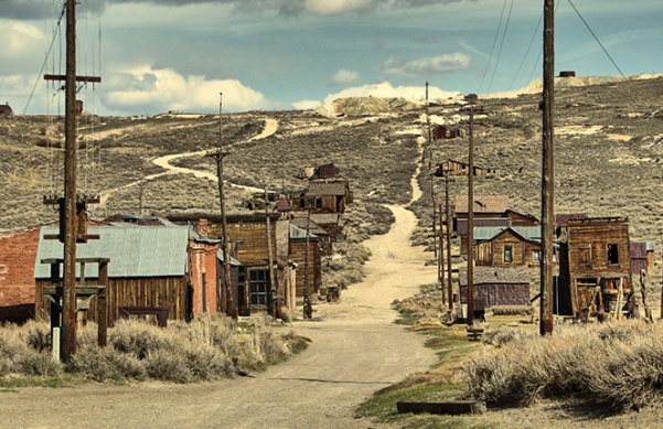 old buildings along a dirt road in the hills (California ghost down of Bodie)