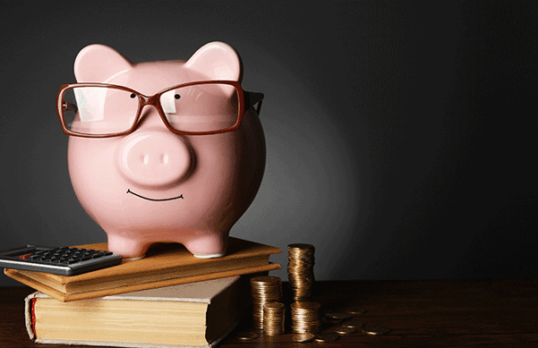 piggybank wearing glasses, on top of books next to a calculator and stacks of coins
