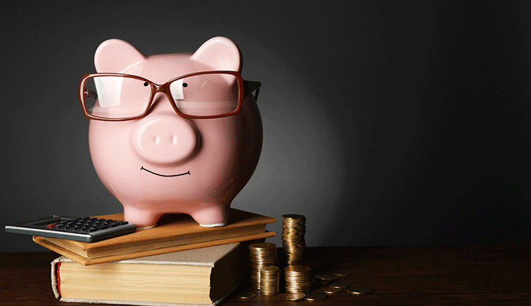 piggybank wearing glasses, on top of books next to a calculator and stacks of coins