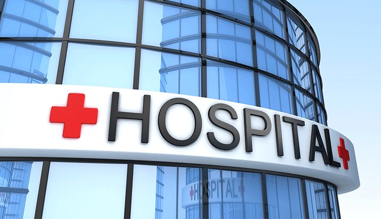 glass cylindrical building with white stripe around it, with a red plus sign and the word Hospital in large black letters