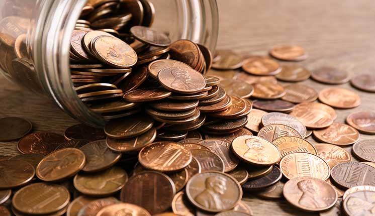 a jar laying on its side with pennies spilling out onto a table