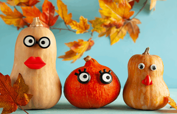winter squash with googly eyes and mouths, surrounded by leaves and in front of a blue wall