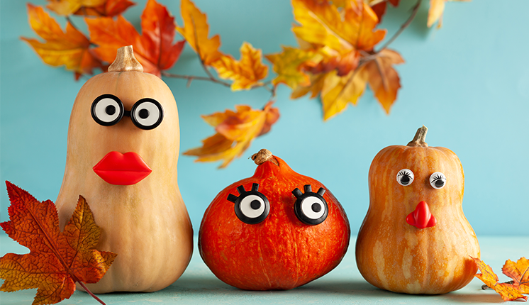 winter squash with googly eyes and mouths, surrounded by leaves and in front of a blue wall